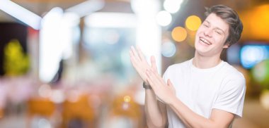 Casual beyaz t-shirt üzerinde izole giyen genç yakışıklı adam arka plan Clapping ve mutlu ve neşeli, gururlu gülümseyen birlikte eller alkış