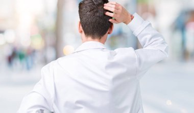 İzole arka plan geriye düşünme hakkında şüphe kafasına el ile üzerine beyaz önlük giyen genç profesyonel bilim adam