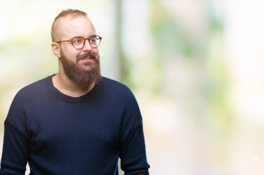 Genç beyaz hipster adam görünümlü yan ve dik dik bakma uzağa düşünce gülümseyen izole arka plan üzerinde güneş gözlüğü takıyor.