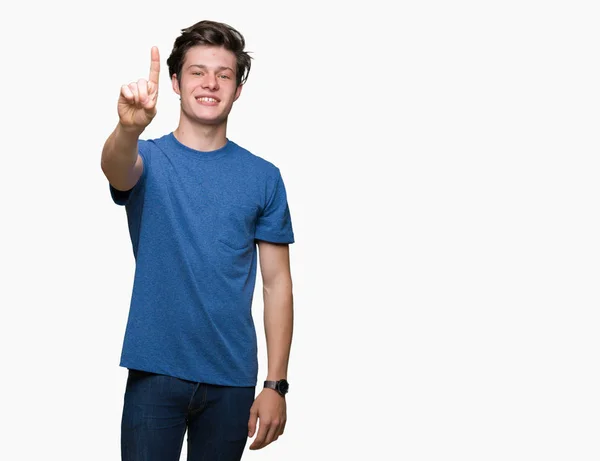 年轻英俊的男人穿着蓝色的 T恤在孤立的背景显示和手指第一 同时微笑着自信和快乐 — 图库照片