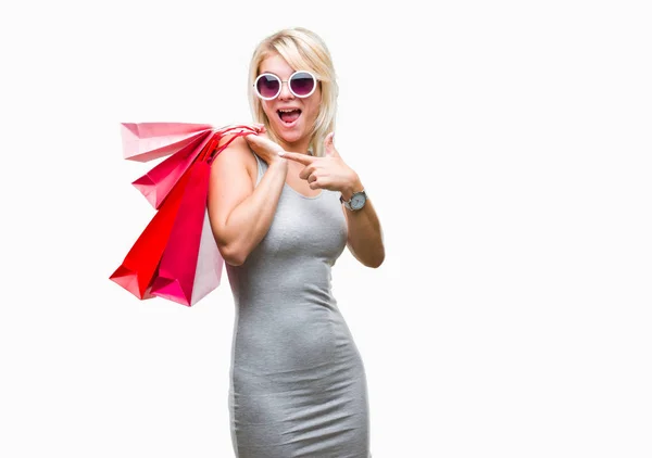 孤立した背景の手と指で指している非常に幸せで持株ショッピング バッグ販売のショッピング若い美しいブロンドの女性 — ストック写真