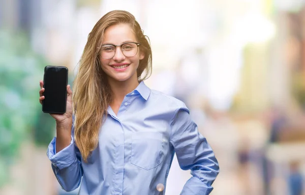 Young beautiful blonde business woman showing screen of smartphone over isolated background with a happy face standing and smiling with a confident smile showing teeth