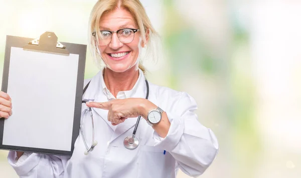 Middle age blonde doctor woman holding clipboard over isolated background very happy pointing with hand and finger