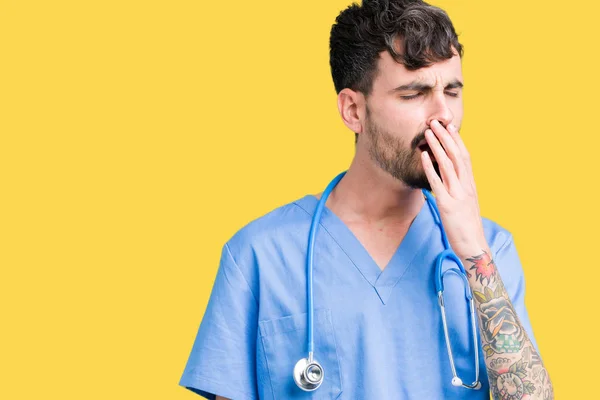 Young handsome nurse man wearing surgeon uniform over isolated background bored yawning tired covering mouth with hand. Restless and sleepiness.