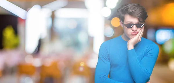 Young man wearing funny thug life glasses over isolated background thinking looking tired and bored with depression problems with crossed arms.