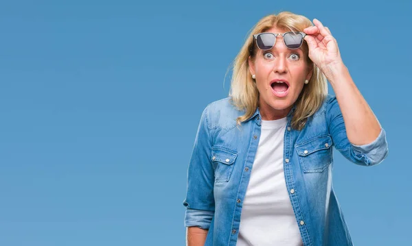 Middle age blonde woman wearing sunglasses over isolated background afraid and shocked with surprise expression, fear and excited face.