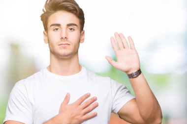 Arka plan üzerinde beyaz t-shirt giyen genç yakışıklı adam izole göğüs ve bir sadakat sözü yemin yapma avuç, el ile küfür