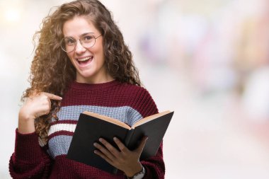 Genç esmer kız kendisi için sürpriz yüz işaret parmağı ile izole arka plan üzerinde gözlük takan bir kitap okuma