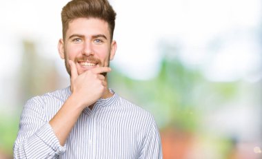 Genç yakışıklı adam emin çapraz kollar ve çeneme kaldırdı el ile gülümseme ile kameraya bakıyor. Pozitif düşünce.