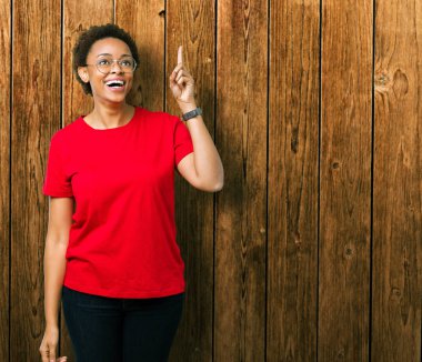 Başarılı fikirle izole arka plan işaret parmağı üzerinde gözlük takan güzel genç Afro-Amerikan kadın. Çıktıktan ve mutlu. Bir numara.