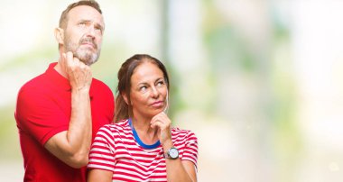 Orta yaş İspanyol çift çene düşünme hakkında soru, dalgın ifade üzerine el ile izole arka plan üzerinde aşık. Düşünceli yüzüyle gülümsüyor. Şüphe kavramı.