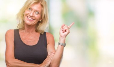 Kameraya bakarak yan el ve parmak ile işaret orta yaş sarışın kadın yüzünde kocaman bir gülümseme ile izole arka plan.