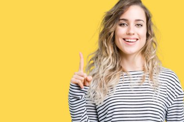 Ve parmak gülümseyen süre bir numara ile kendinden emin ve mutlu yukarıyı gösteren izole arka plan üzerinde çizgili süveter giyen güzel genç sarışın kadın.