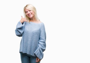 İşin gülümseyen izole arka plan üzerinde kış kazak giyen genç güzel sarışın kadın telefon hareketi ile el ve parmak telefonda konuşuyor gibi. Kavramları iletişim.