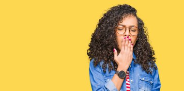 Kıvırcık saçlı gözlüklü genç güzel kadın el ağzıyla kapsayan yorgun esneme sıkılmış. Restless ve uyku hali.