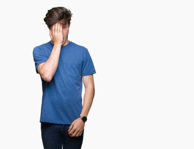 Yarım yüz, göz ve ağız el ile kapsayan yorgun esneme izole arka plan üzerinde mavi t-shirt giyen genç yakışıklı adam. Acı yüzü acıyor.