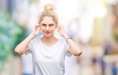 Yüksek sesle müzik gürültü rahatsız ifade parmaklarıyla kulaklarıyla kapsayan izole arka plan üzerinde beyaz t-shirt giyen genç güzel sarışın kadın. Sağır kavramı.