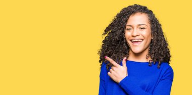 Kıvırcık saçlı kış kazak neşeli bir gülümseme ile el ve parmak kadar yan yüzünde mutlu ve doğal ifade ile işaret yüz giyen genç güzel kadın