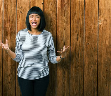 Üzerinde çizgili süveter giyen güzel genç Afro-Amerikan kadın arka plan deli izole ve deli bağırarak ve agresif ifade ve silah kaldırdı bağırıyor. Hayal kırıklığı kavramı.