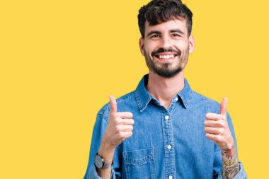 Yakışıklı delikanlı izole arka plan başarı işareti el ile pozitif jest yapıyor üzerinde başparmak gülümseyen ve mutlu. Neşeli bir ifadeyle, kazanan jest kameraya bakıyor.