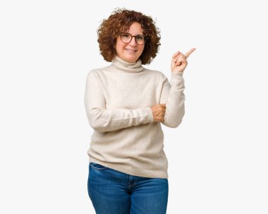 Kameraya bakarak yan el ve parmak ile işaret eden balıkçı yaka kazak ve gözlük yüzünde kocaman bir gülümseme ile izole arka plan üzerinde giyen güzel orta ager üst düzey kadın.