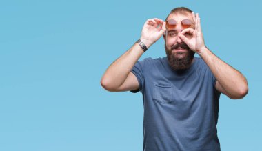 Genç beyaz hipster adam gülümsüyor, parmakları ile mutlu yüz üzerinden seyir göz el ile ok jest yapıyor izole arka plan üzerinde güneş gözlüğü takıyor.