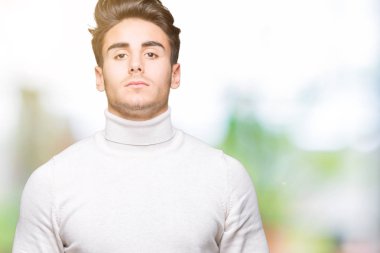 Yüzünde ciddi bir ifade ile izole arka plan üzerinde boğazlı kazak giyen genç yakışıklı adam. Basit ve doğal kameraya bakıyor.