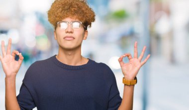 Afro gözlük sakin ol genç yakışıklı adamla ve gülümseyen gözlerle parmak ile meditasyon jest yapıyor kapalı. Yoga kavramı.