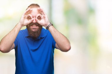 Dilini, parmaklarının arasından baktığını yapışmasını dürbün gibi ok jest yapıyor izole arka plan üzerinde mavi gömlek giymiş genç beyaz hipster adam. Deli ifade.