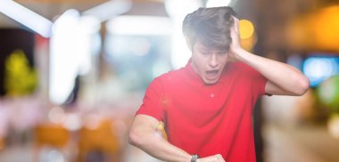 Üzerinde kırmızı t-shirt giyen genç yakışıklı adam arka plan izole seyretmek zaman endişeli, geç korkuyor arıyorsunuz