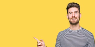 Kameraya bakarak yan el ve parmak ile işaret yüzünde kocaman bir gülümseme ile kazak giyen genç yakışıklı adam çizgili.