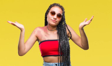 Genç izole arka plan clueless ve şaşkın bir ifadeyle kollar ve eller kaldırdı üzerinde güneş gözlüğü takıyor Doğum işareti ile Afrikalı-Amerikalı saç örgülü. Şüphe kavramı.