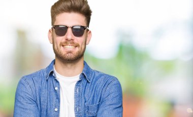 Denim ceket ile mutlu yüz gülümseyen giyen genç yakışıklı zarif adam kameraya seyir silah geçti. Olumlu bir kişi.