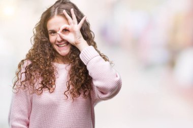 Güzel esmer kıvırcık saçlı Genç kız giyiyor pembe kış kazak gülümseyen, parmakları ile mutlu yüz üzerinden seyir göz el ile ok jest yapıyor izole arka plan üzerinde.