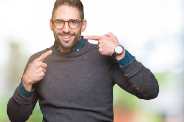Kendinden emin gösterilen ve işaret parmakları diş ve ağız ile gülümseyen izole arka plan üzerinde gözlük takan yakışıklı delikanlı. Sağlık kavramı.
