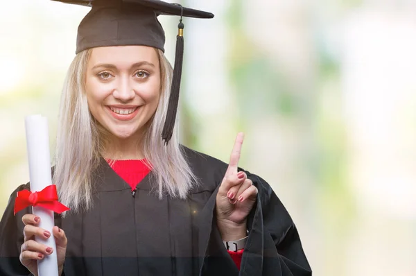 幸せそうな顔 ナンバーワンのアイデアや質問ポインティング指と分離の背景の上の学位を保持する大学院の制服を着て若いブロンドの女性を驚かせた — ストック写真