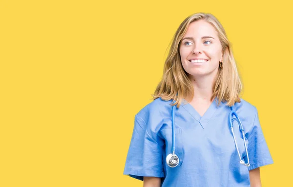 美丽的年轻医生妇女穿着医疗制服在孤立的背景看着一边面带微笑 自然的表情 笑自信 — 图库照片