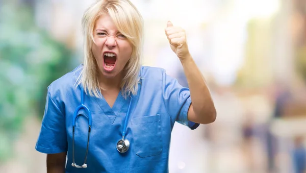 怒ってい イライラして怒りで叫びながら激怒の拳を上げる狂牛病分離の背景に医療制服を着て美しい金髪女医女性 怒りと攻撃的な概念 — ストック写真