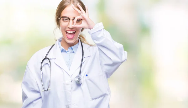 美丽的年轻的金发医生妇女穿医疗制服在孤立的背景做 手势与手微笑 眼睛看通过手指与幸福的脸 — 图库照片