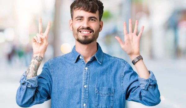 Yakışıklı delikanlı gösterilen ve parmakları ile işaret izole arka plan üzerinde kendinden emin ve mutlu gülümseyerek süre yedi numara.
