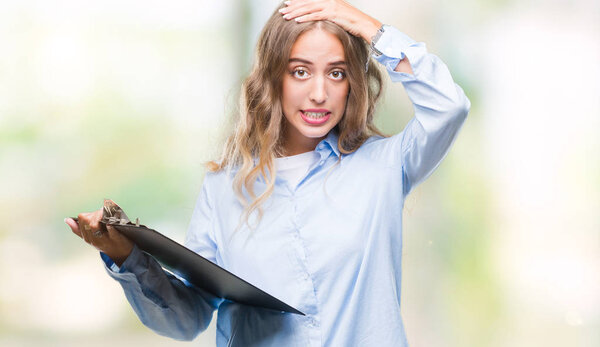 Beautiful young blonde business woman holding clipboard over isolated background stressed with hand on head, shocked with shame and surprise face, angry and frustrated. Fear and upset for mistake.