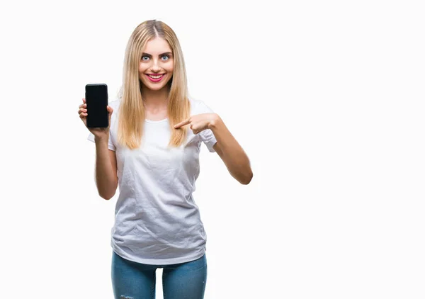 Young beautiful blonde woman showing smartphone over isolated background with surprise face pointing finger to himself