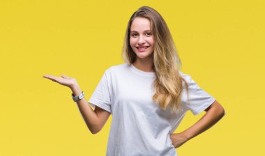 Neşeli sunulması ve kameraya bakarak avucunun ile işaret gülümseyen izole arka plan üzerinde rahat beyaz t-shirt giyen genç güzel sarışın kadın.