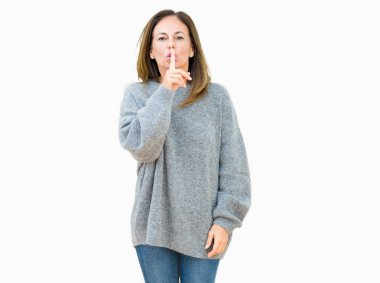 Dudaklarında parmak ile sessiz olmanı izole arka plan üzerinde kış kazak giyen güzel orta yaş kadın. Sessizlik ve gizli kavramı.