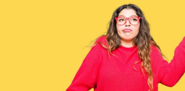 Kırmızı giyen genç güzel kadın clueless ve şaşkın bir ifadeyle kollar ve eller kaldırdı gözlük. Şüphe kavramı.