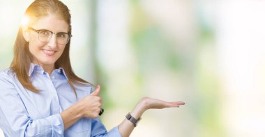 İzole arka plan gösteren palm el üzerinde gözlük takan ve yukarıya, mutlu ve neşeli gülümseyen baş parmakları Tamam jest yapıyor güzel orta yaş olgun iş kadını