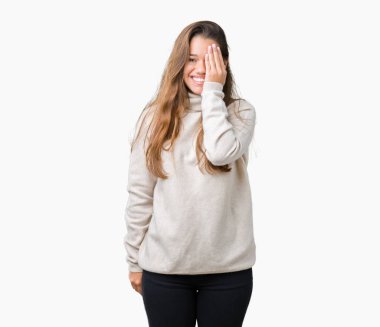 El yüz ve sürpriz duygu kendinden emin gülümseme ile tek gözüyle kapsayan izole arka plan üzerinde boğazlı kazak giyen genç güzel esmer kadın.