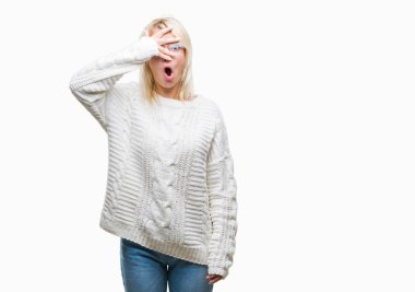 Mahcup ifadeyle parmaklarımın arasından seyir kış kazak ve gözlük yüz ve gözler el ile kapsayan şok izole arka plan bakmak üzerinde giyen genç güzel sarışın kadın.