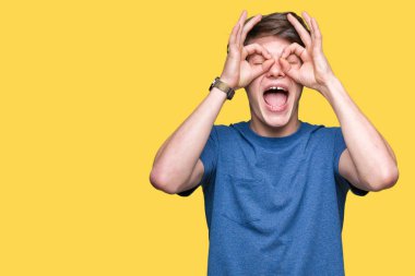 Dilini, parmaklarının arasından baktığını yapışmasını dürbün gibi ok jest yapıyor izole arka plan üzerinde mavi t-shirt giyen genç yakışıklı adam. Deli ifade.