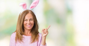 Kameraya bakarak yan el ve parmak ile işaret Paskalya tavşan kulakları yüzünde kocaman bir gülümseme ile izole arka plan üzerinde giyen orta yaş esmer kadın.